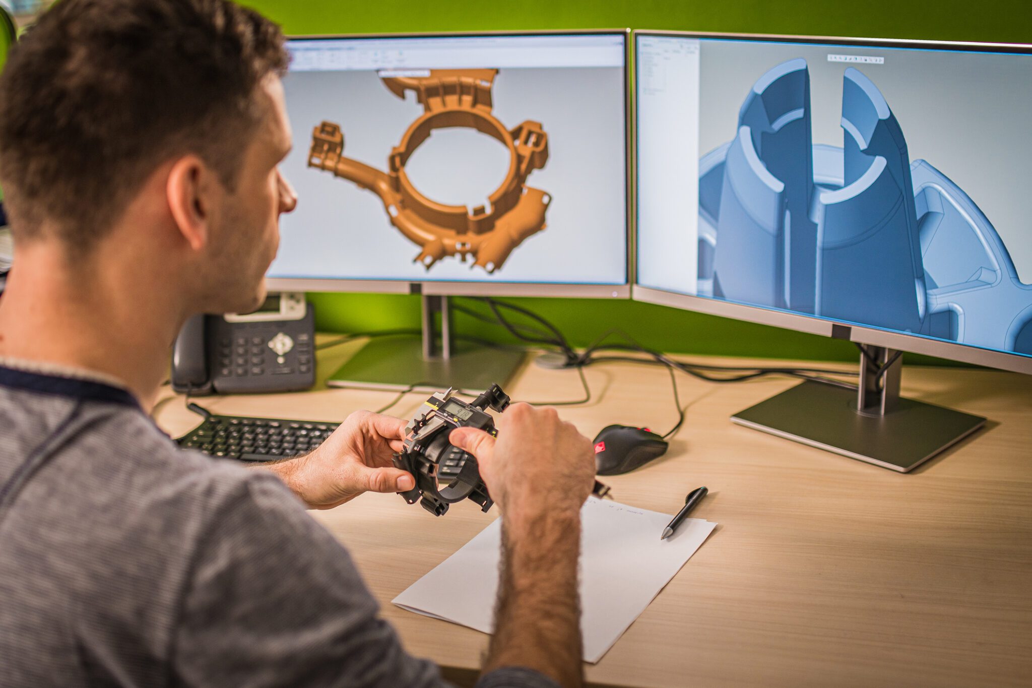 Design engineer working at his computer while holding a 3D part to gain better perspective while innovating high quality custom metal components